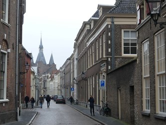 <p>Een doorkijkje in westelijke richting door de Koetsraat maakt het goed voorstelbaar dat hier, ongeveer 10 meter achter de huidige (rechter) rooilijn, een stadsmuur heeft gelopen die doorliep tot aan de in 1409 voltooide Sassenpoort. Rechts het statige pand van de Groote Sociëteit.</p>
